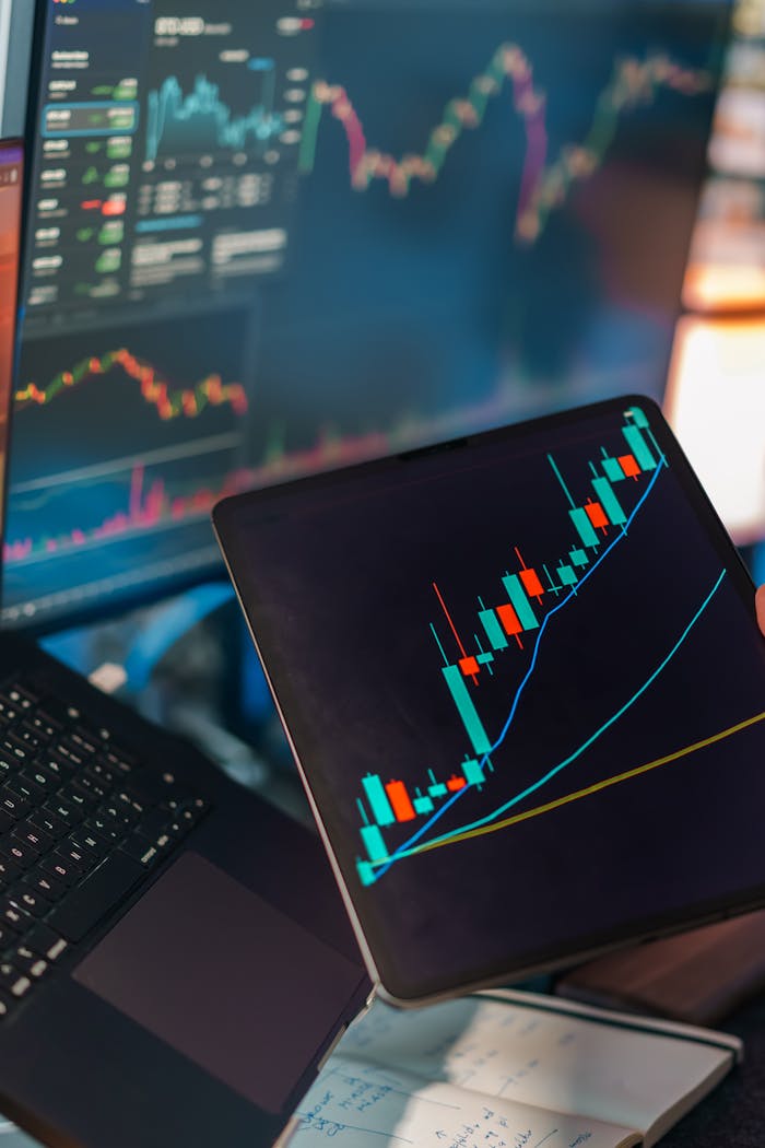 about-02 A tablet displaying a candlestick chart with a laptop screen showing stock market data for financial analysis.